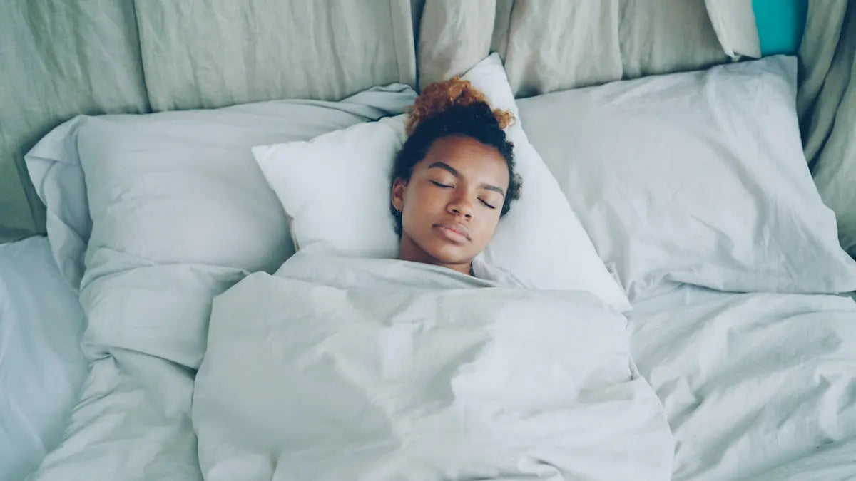 A young woman sleeping peacefully in a white bed.
