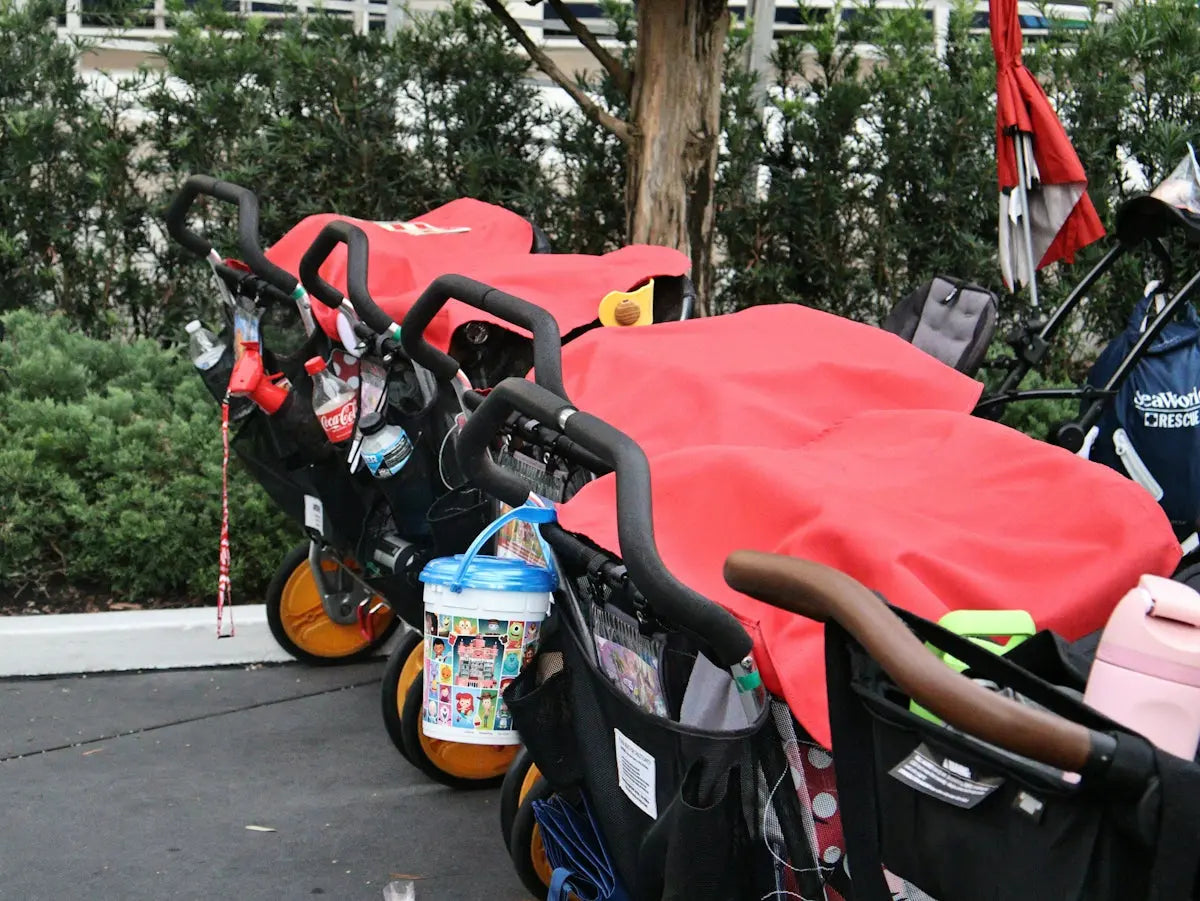Several baby strollers with red covers parked outdoors.